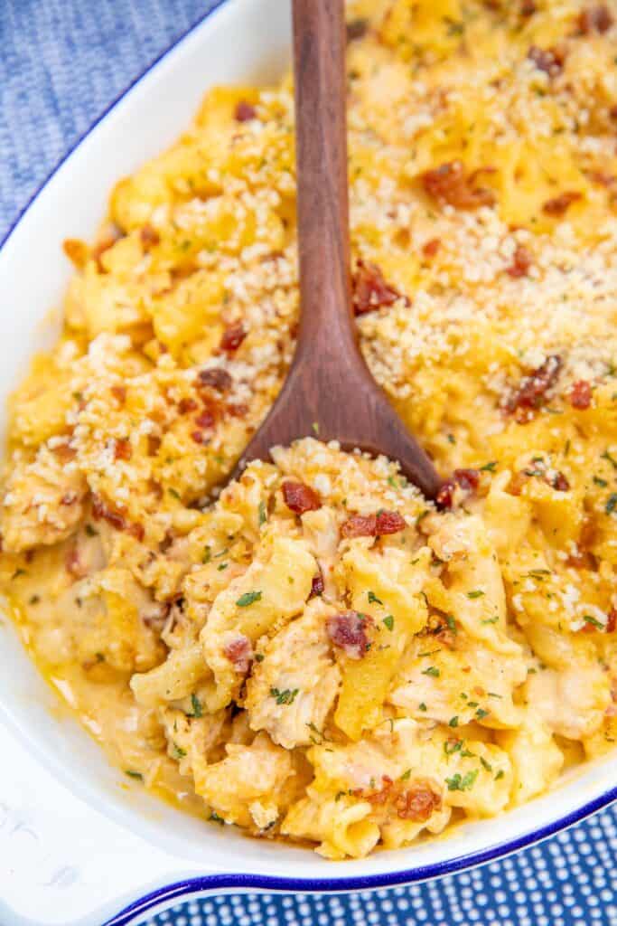 scooping chicken macaroni and cheese from a baking dish with a wooden spoon