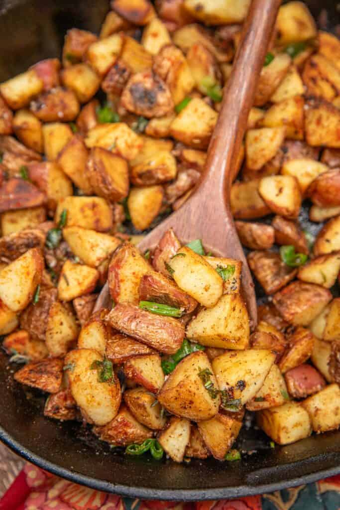 scooping home fries from a skillet with a wooden spoon